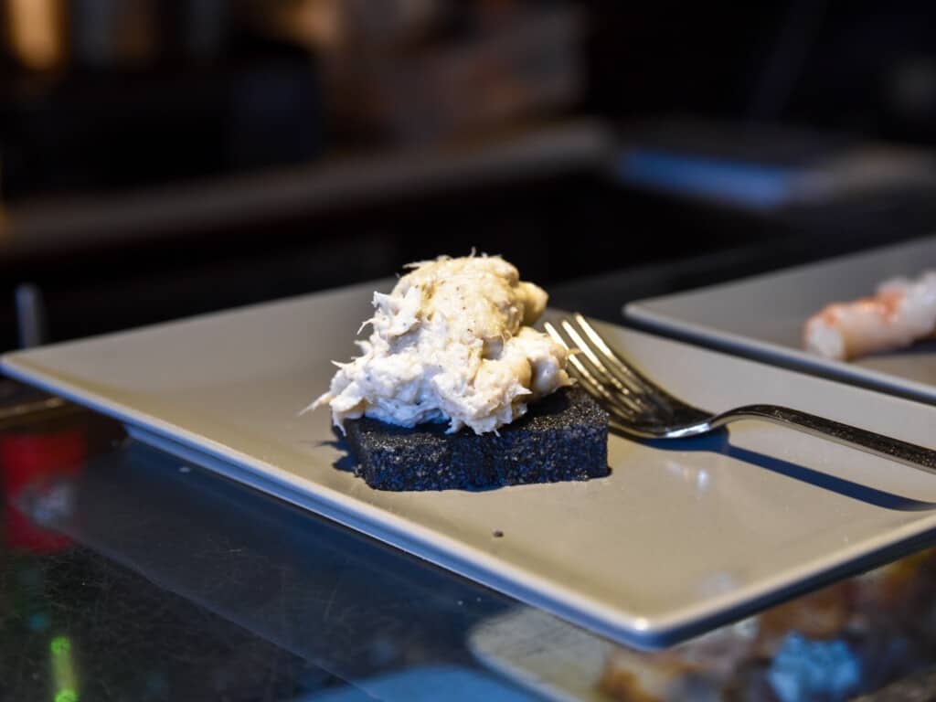 Grey, rectangular plate on a glass table holds a gluten-free cicchetto with a fish spread in Venice, Italy.