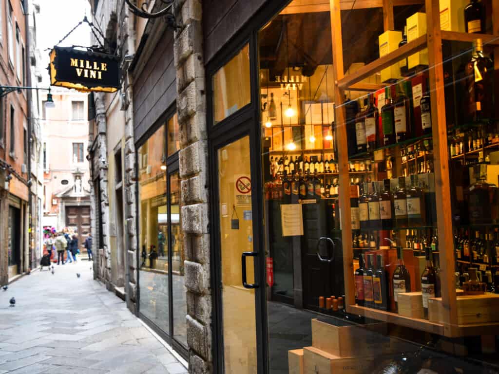 Entrance and window display at Mille Vini in Venice, Italy. Wines in the window and a few people in the end of the street on left of entrance.
