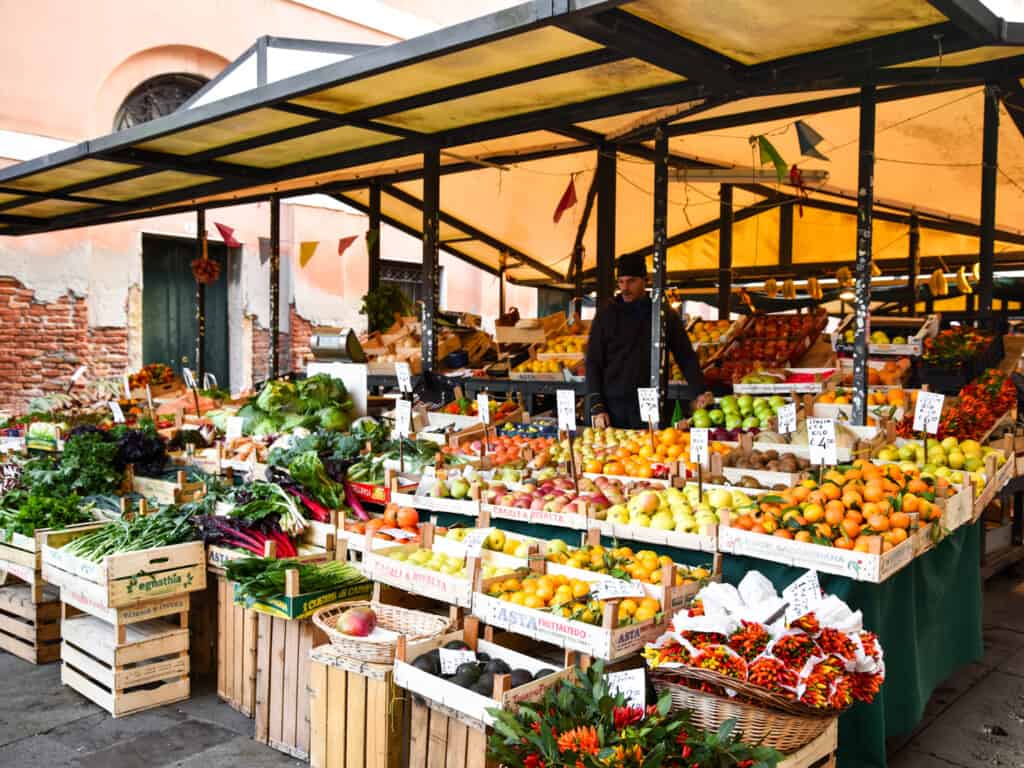 Booth and worker with stand of fresh fruits and vegetables at the Rialto Market in Venice, Italy.