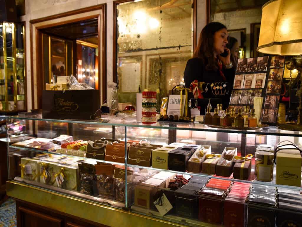 Gourmet packages of food to take as souvenirs are behind a glass display at Florian in Venice, Italy. Woman behind counter talks on the phone.