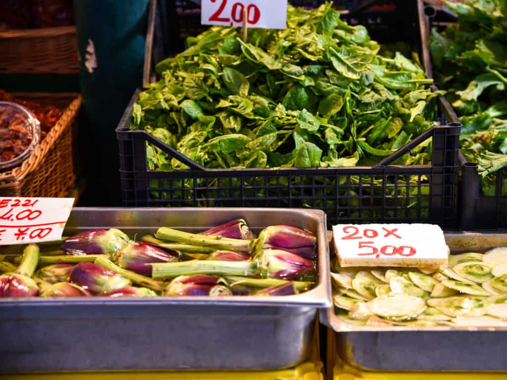 Plastic and metal bins of spinach, artichokes and fresh veggies at the Rialto Market in Venice, Italy.