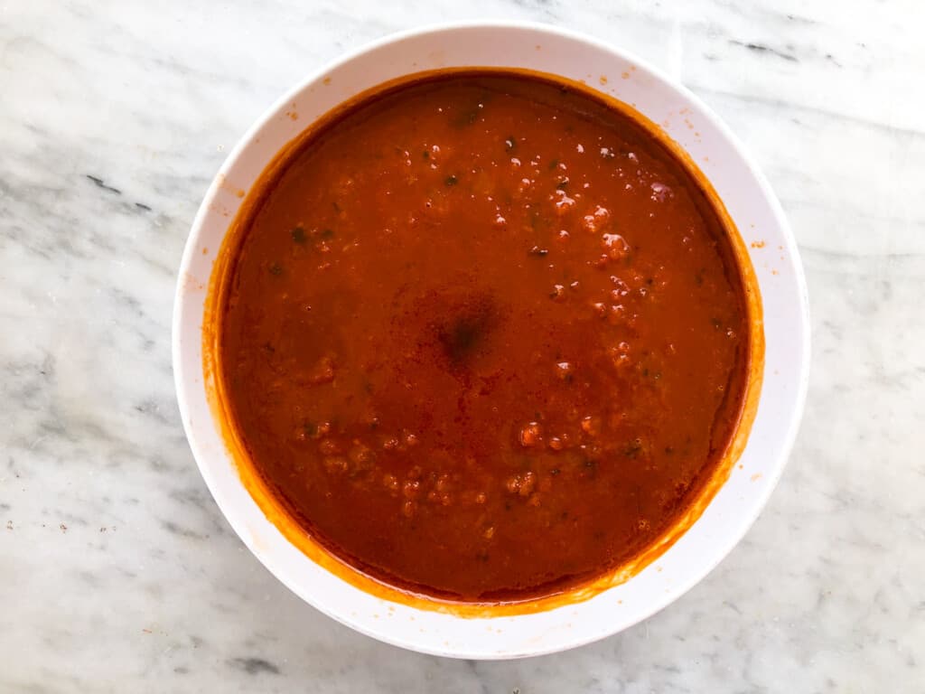 White bowl full of fresh pomodoro sauce sitting on white marble surface, as seen from above.