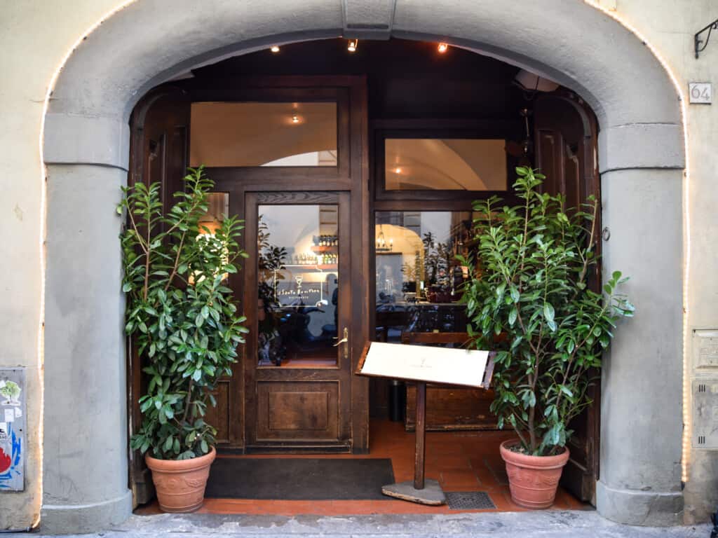 Main entrance to Il Santo Bevitore in Florence, Italy. Wooden doorway with glass windows and plants on either side of door.