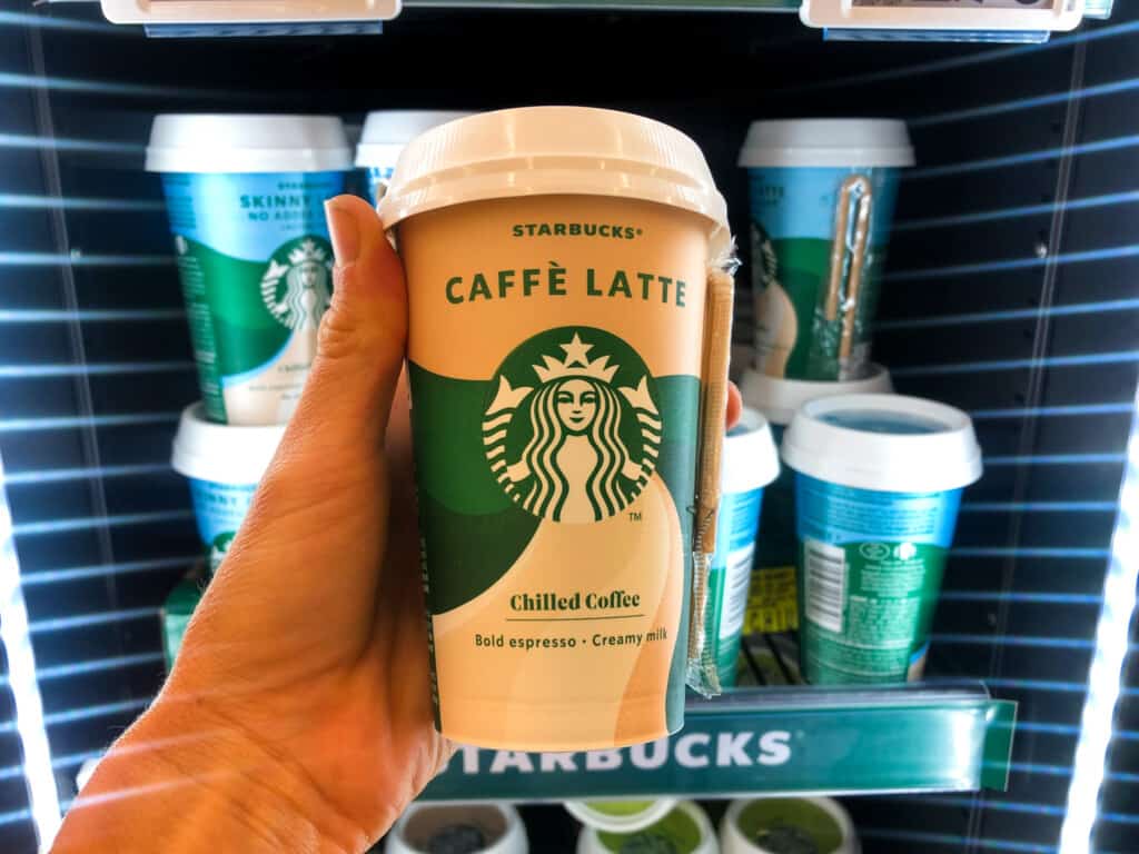 Hand holding refrigerated caffè latte cup in front of display at Starbucks in Italy.