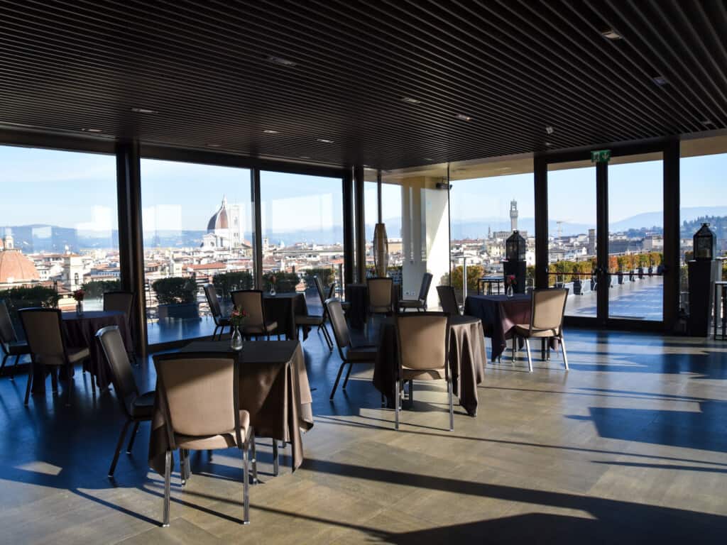 Rooftop bar with large glass windows and view of Duomo in Florence, Italy.