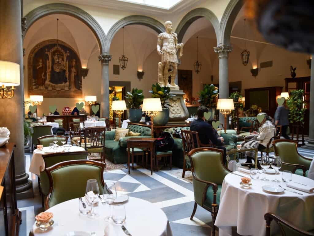 Dining room at upscale restaurant in Florence, Italy. Statue in the middle of the room, tables with white tablecloths, arches around the room.