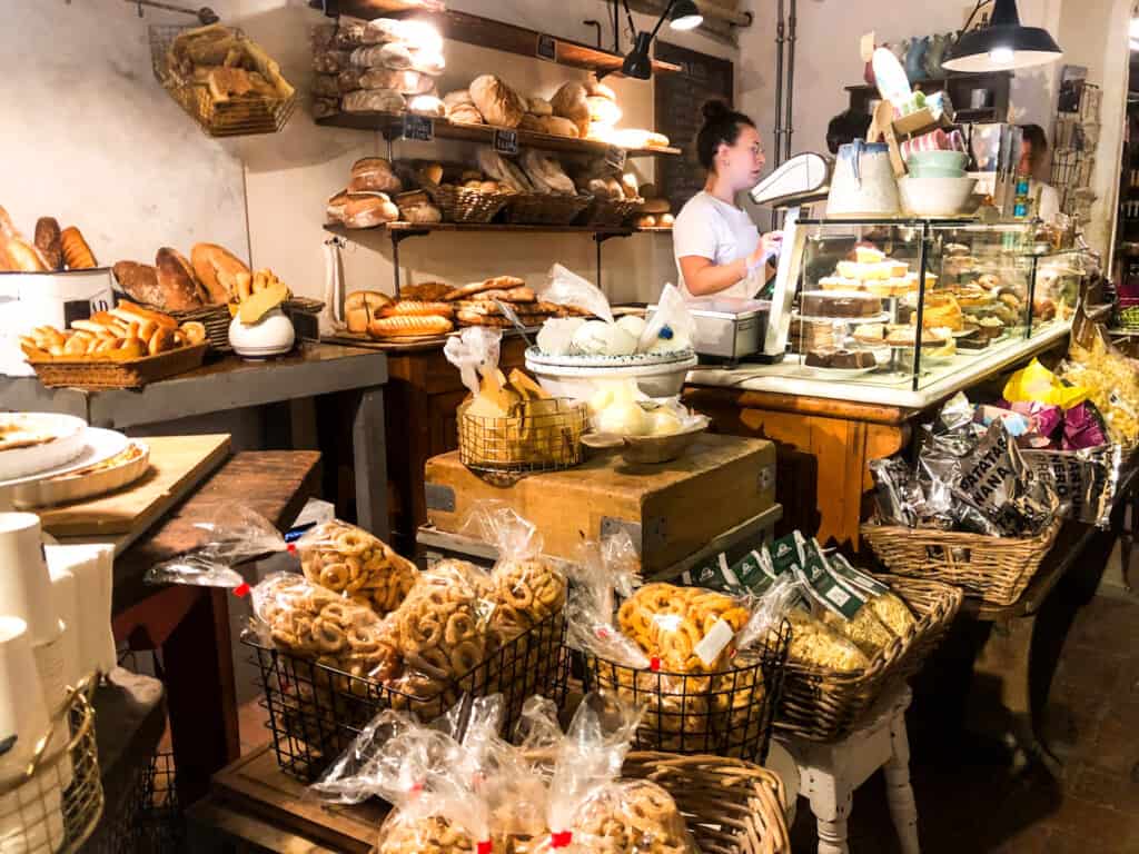 Woman at cash register at bakery in Florence, Italy. Breads and other baked goods in baskets and on display all around her.