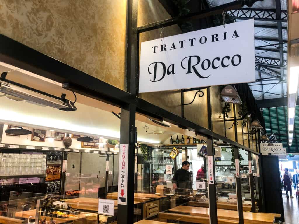 Sign at Trattoria da Rocco in Florence, Italy. Wooden tables set up in restaurant.