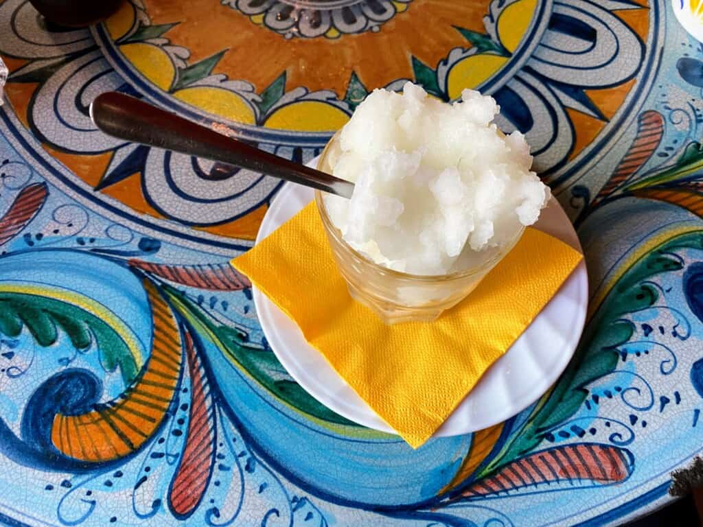 Lemon granita sitting on a napkin and small white plate on top of a colorful tile table.