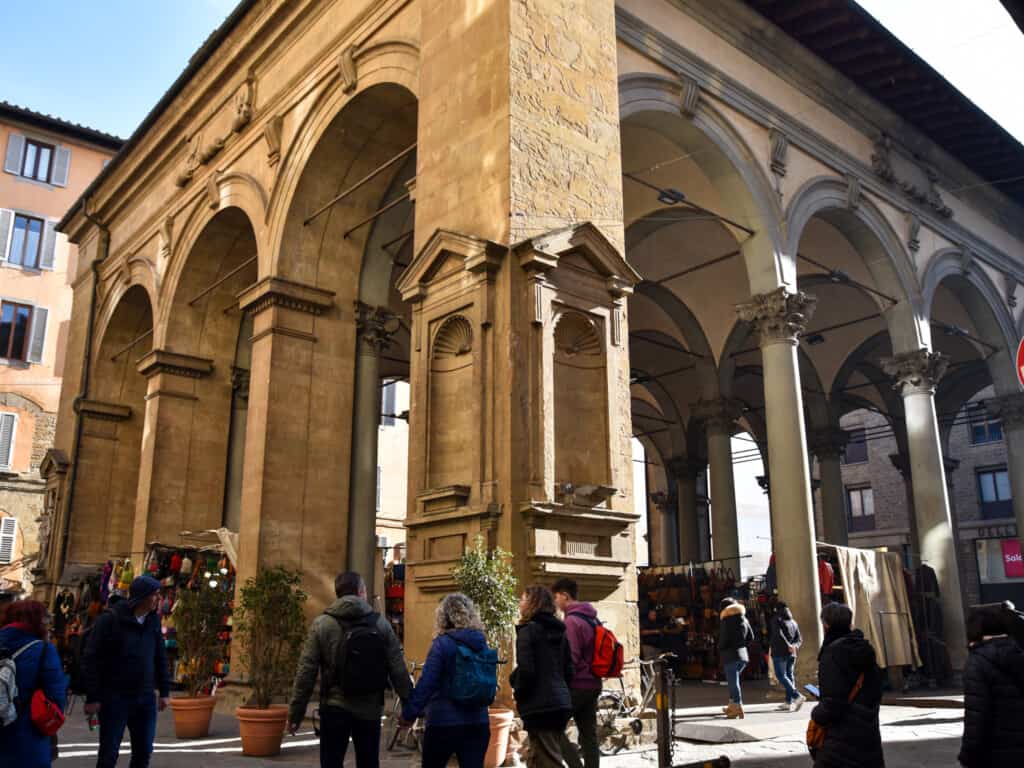 Angled side view of large porcellino market in Florence with large stone structure with people walking under it. 