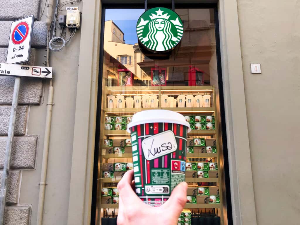 hand holding up of coffee with Starbucks window in background.