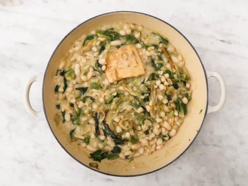 Pot with cannellini beans, greens, and parmesan cheese rind.