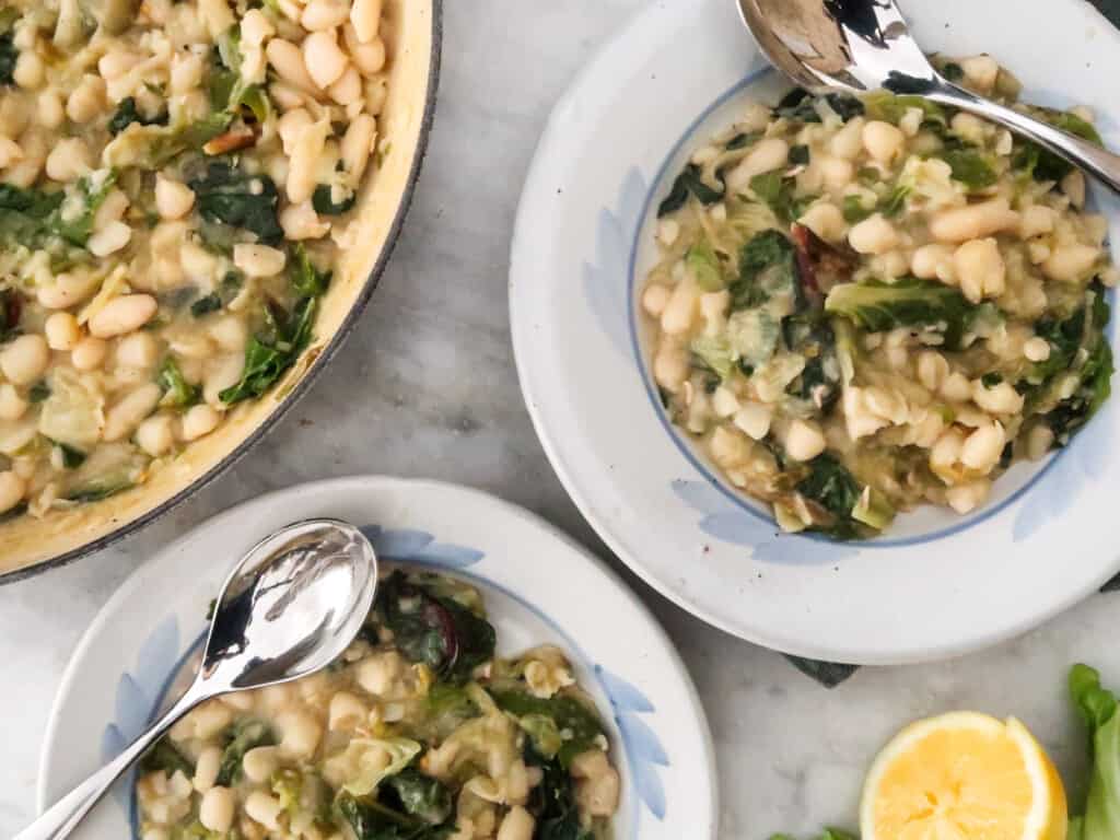 Plates with greens and beans next to large pot with them and a sliced lemon.