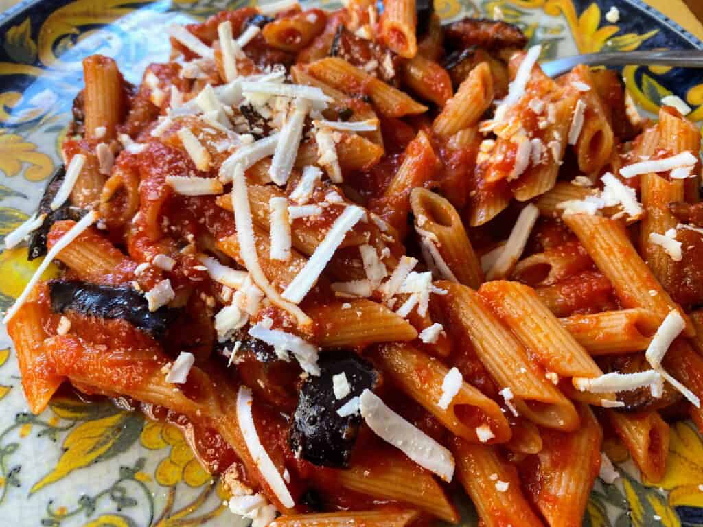 Plate of penne pasta with norma sauce on a ceramic plate. Shredded ricotta salata sprinkled on top.