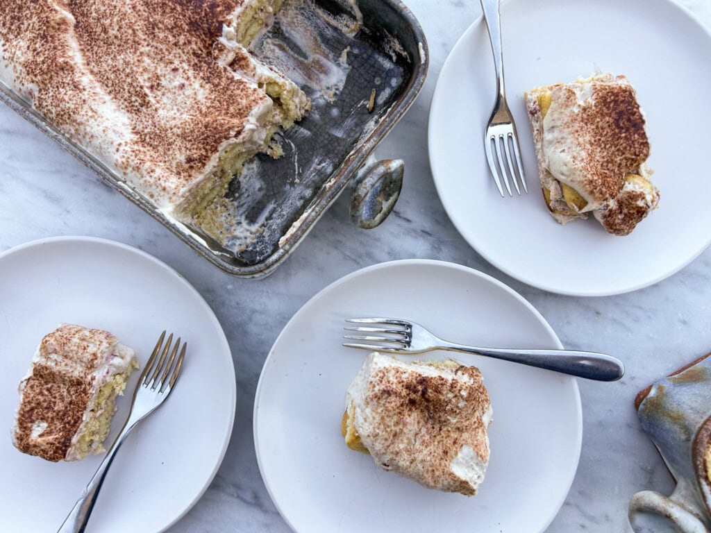 Delicious homemade tiramisu served with forks on white plates, featuring layers of coffee-soaked ladyfingers and mascarpone cheese.