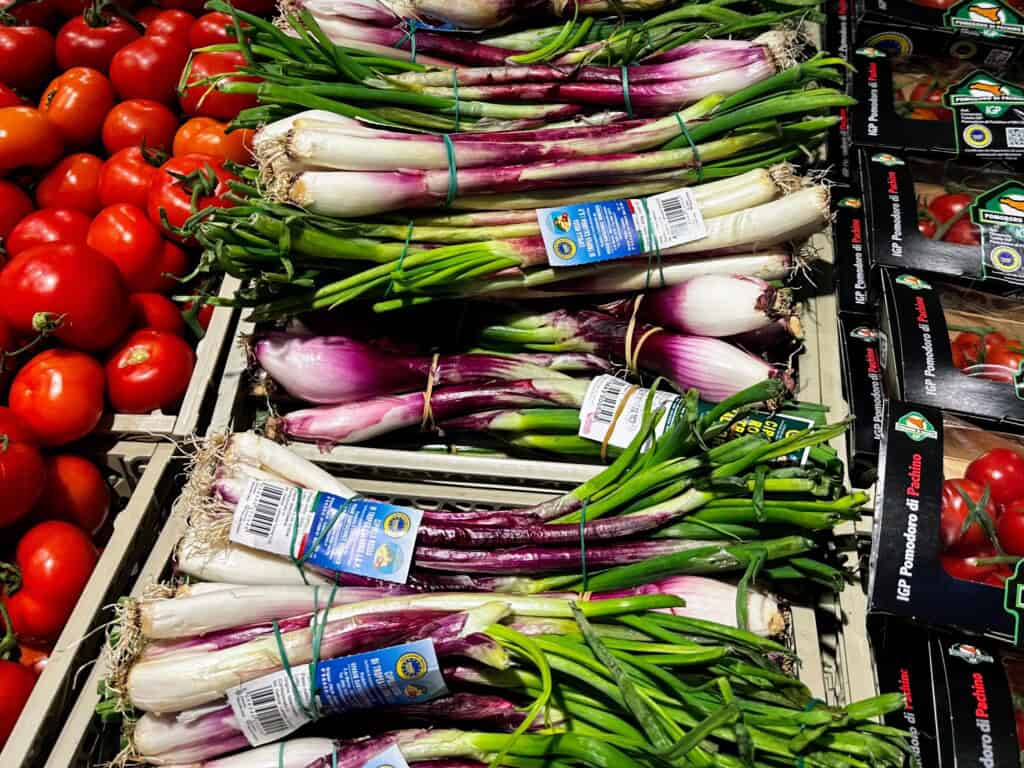 Tropea onions piled next to tomatoes, for sale at a grocery store in Italy.